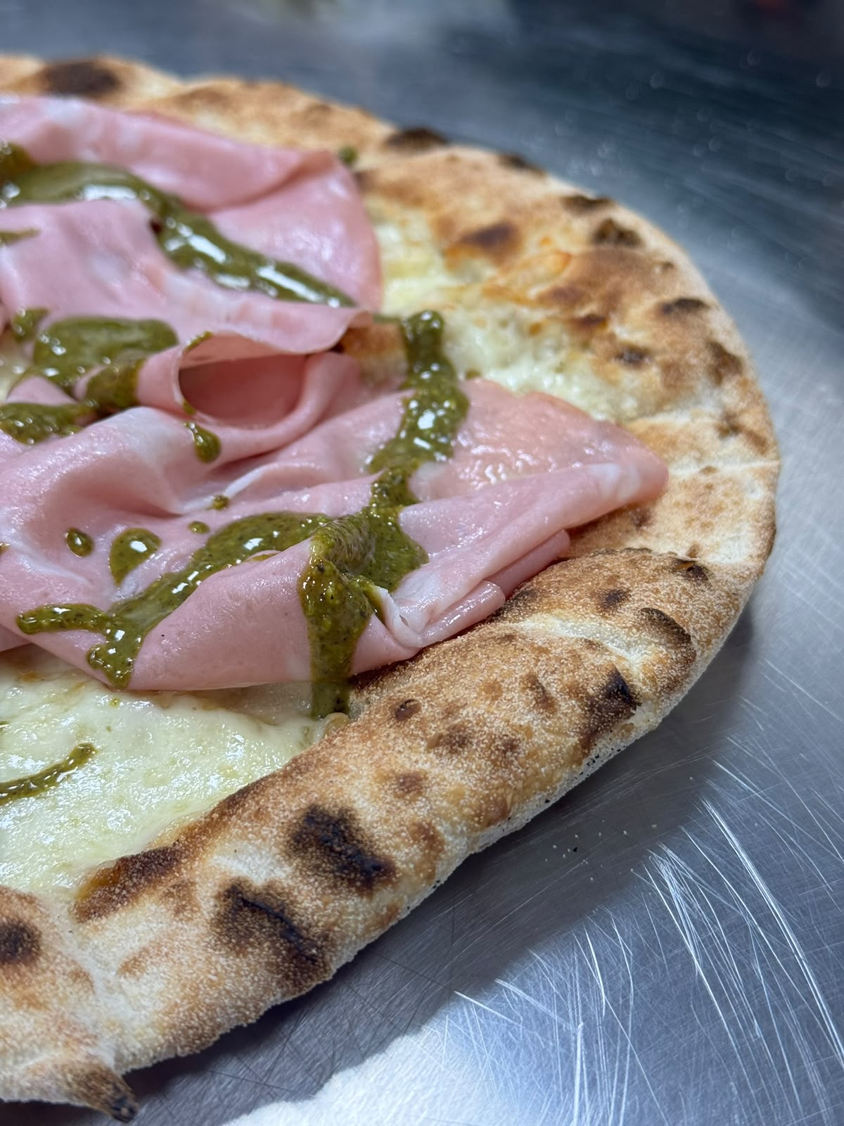Close-up of mortadella and pesto on a blistered Italian Secret crust